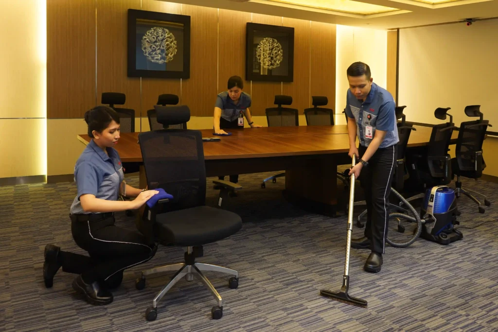 Cleaning staff vacuuming and wiping a conference room.