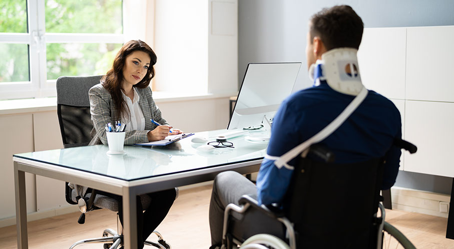 A professional speaks with a person in a wheelchair wearing a neck brace during a consultation